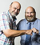Two older bald men with beards fist bumping and smiling at the camera
